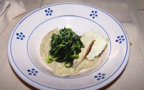 Piatto con fave e cicoria saltata, guarnito con una scaglia di formaggio e un'acciuga.