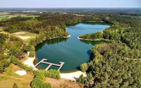 Malownicze jeziora w Zielonej Górze otoczone lasem, z drewnianym pomostem i piaszczystą plażą. Idealne miejsce na wypoczynek.