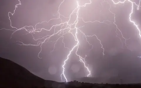 Éclairs zébrant un ciel sombre, illuminant un paysage montagneux lors d'un photo d'orage spectaculaire.