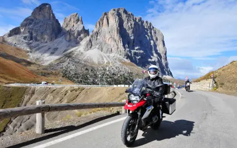 Motocyklista przemierza malowniczą drogę w Dolomitach. Pogoda dopisuje, a widoki zapierają dech w piersiach.