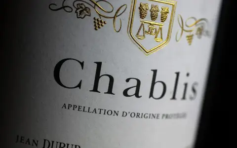 Étiquette de vin Chablis, avec un blason doré orné de grappes de raisin et d'une balance. L'appellation d'origine protégée évoque le vignoble de Chablis.