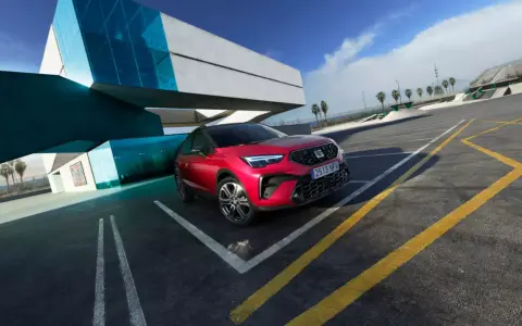 Czerwony Seat Arona, jeden z najnowszych seat modele, zaparkowany przy nowoczesnym budynku z niebieskimi akcentami.