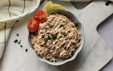 Un bol de rillettes de thon, garni de tomates cerises et de quartiers de citron, prêt à être dégusté.