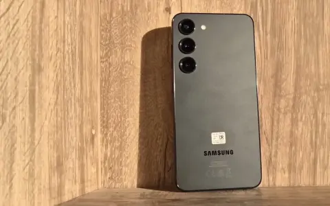 Szary Samsung S23 z trzema obiektywami aparatu na drewnianym tle. Długo działająca bateria pozwoli Ci cieszyć się nim przez cały dzień.