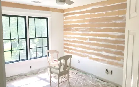 Room in progress, showing how to install shiplap on the wall. Two chairs sit on protective plastic sheeting.