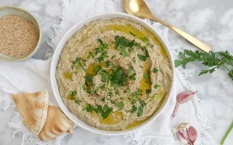 Crema de berenjena asada con aceite de oliva, perejil y semillas de sésamo, servida con pan de pita.