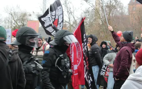 Demonstranten mit Fahnen, darunter eine mit der Aufschrift "System Metternich", und Polizisten in Schutzkleidung.