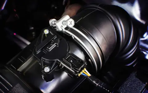 Detalle de un sensor MAF negro conectado a un tubo de admisión de aire. Este componente es clave para saber qué es el sensor MAF y cómo optimiza el rendimiento del motor.