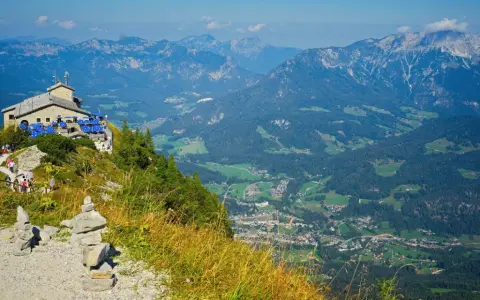 View from Hitler's Eagle's Nest, a stone building with blue umbrellas, perched high in the Bavarian Alps overlooking a valley.