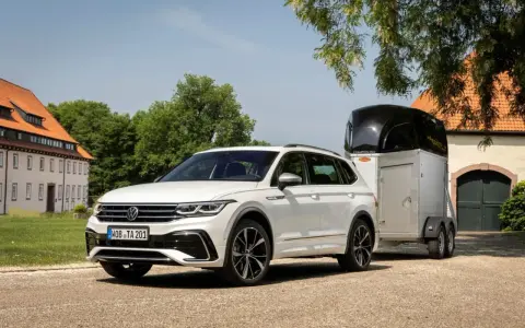 Biały Volkswagen SUV z przyczepą do przewozu koni stoi przed starym budynkiem.