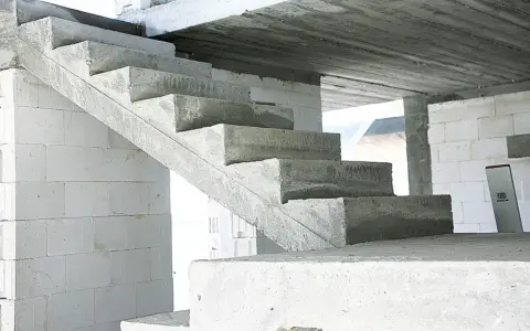 Surowe, betonowe schody czekają na wykończenie. W tle białe bloczki budowlane.