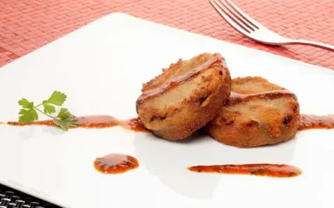 Dos manitas de cerdo rebozadas y fritas, servidas con salsa roja y perejil en un plato blanco.