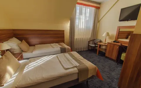 Pokój w zajazd u dziadka: dwa wygodne łóżka, stolik nocny z lampką, biurko z lustrem i krzesłem, telewizor.