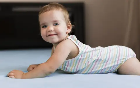 Un adorabile neonato di 8 mesi, con occhi azzurri e un sorriso contagioso, gioca sul letto.