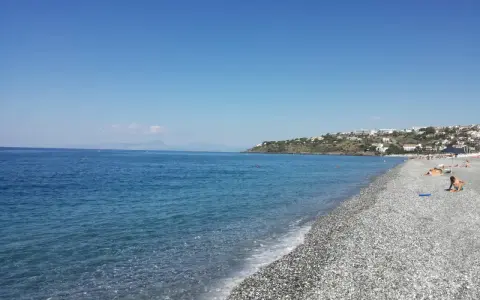 Spiaggia di ciottoli con mare azzurro e case arroccate sulla collina. Una giornata perfetta per godersi la **scalinea mare**.
