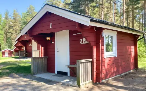 Röda stugor med vita knutar vid Gränna camping. En vit dörr och ett fönster syns på stuga nummer 1.