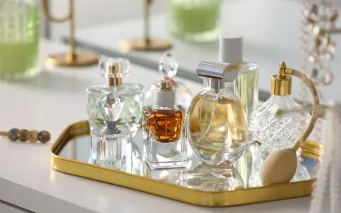 Kolekcja flakonów z płynną esencją perfum, w tym jeden z atomizerem, na złotym lustrzanym tacy.