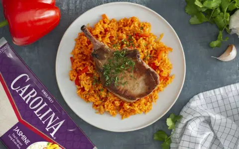 Chuleta de cerdo jugosa sobre arroz rojo con pimientos.