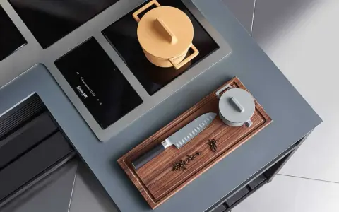 Cuisine moderne avec plaque de cuisson intégrée. Un couteau de chef et des épices sur une planche à découper en bois. Une casserole jaune sur la plaque.
