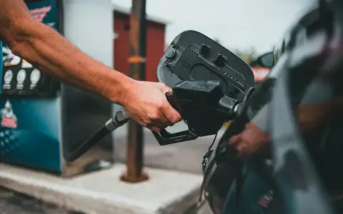 Ręka trzymająca pistolet paliwowy przy otwartym wlewie paliwa. Proces tankowania, jak spuścić paliwo z baku, jest w toku.