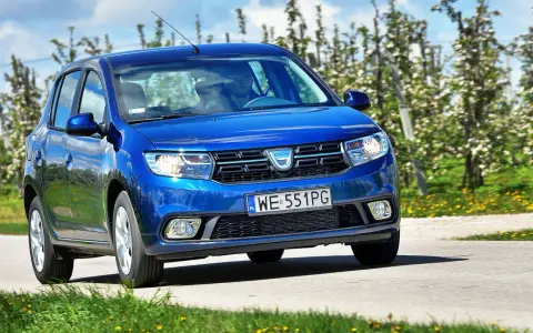 Niebieska Dacia Sandero 2025 jedzie przez kwitnący sad.