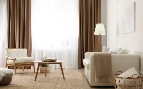 Salon cosy avec 1 ou 2 rideaux par fenêtre, fauteuil en bois, canapé blanc, table basse et tapis en jute.