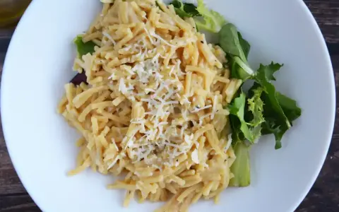 Pyszne cacio e pepe z tartym serem i świeżą sałatką na białym talerzu.