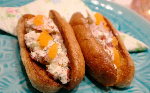 Två lyxiga lobster rolls med krämig fyllning, krispig gurka och orange rom på ett turkost fat.