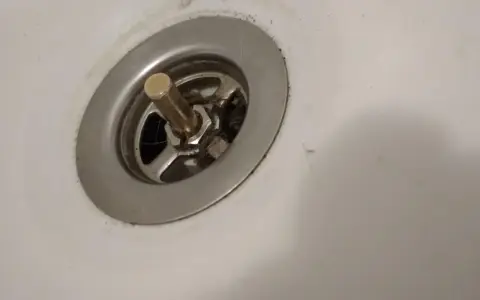 Metalowy korek do wanny z pokrętłem, widoczny mechanizm i włosy. Potrzebna naprawa.