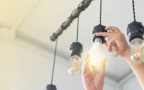 Main d'une personne installant une ampoule gradable dans un lustre.