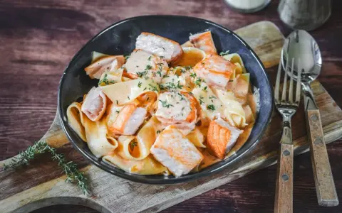 Breite Bandnudeln mit saftigen Lachs-Stücken in cremiger Lachs Sahne Sauce, garniert mit frischen Kräutern. Ein Genuss!