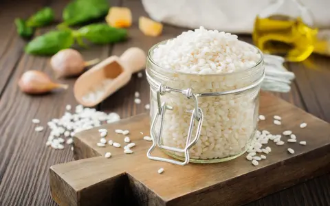 Słoik z ryżem do risotto, drewniana deska, czosnek, bazylia i oliwa.