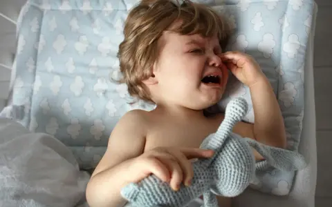 Kleines Kind weint im Schlaf, hält seinen Kuschelhasen fest. Tränen laufen über die Wangen, ein trauriger Moment.