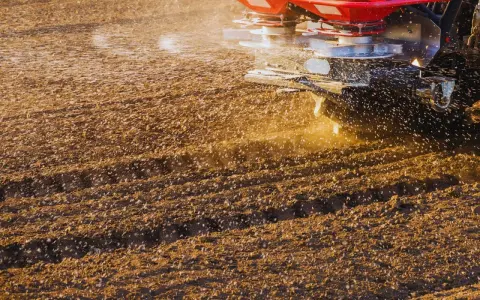 Rozsiewacz aplikuje nawóz na pole. Czy wapno budowlane nadaje się do odkwaszenia gleby? Rolnik dba o żyzność ziemi.