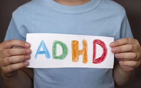 Mani di bambino tengono un foglio con la scritta "ADHD" colorata. Riconoscere i sintomi dell'ADHD è il primo passo.
