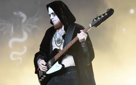Le bassiste d'un groupe metal connu, maquillé et tatoué, joue sur scène, drapé dans une cape noire.