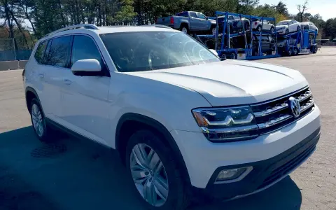 Biały VW Atlas stoi na parkingu, w tle widać lawetę z innymi samochodami.