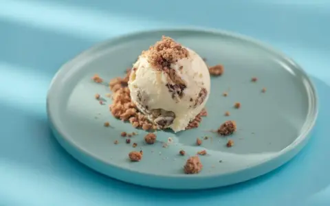Eiscreme mit Schokoladenstückchen und Krümeln, serviert auf einem blauen Teller. Glukosesirup sorgt für die cremige Konsistenz.