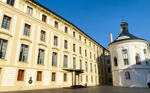 Zamek na Hradczanach, z jego długą, kremową fasadą i okrągłą, białą kaplicą, prezentuje się majestatycznie pod błękitnym niebem.