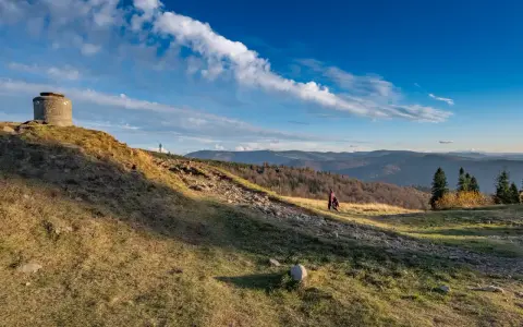 Na zboczu **blatniej góry** stoi betonowy bunkier. W oddali widać pasmo górskie i lasy.