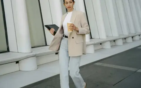 Frau im smart casual Dresscode mit Blazer, Jeans und Kaffee. Sie hält ein Tablet.