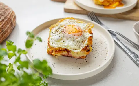 Pyszny croque madame z jajkiem sadzonym na wierzchu, na talerzu, obok chleba i zielonych liści.