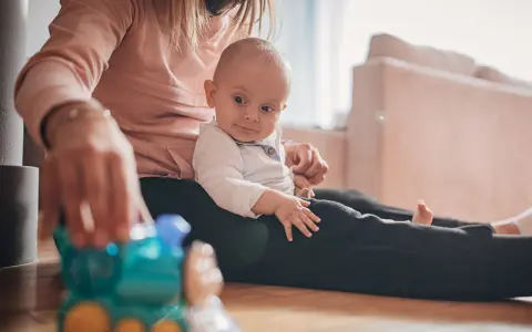 Mama bawi się z 9-miesięcznym dzieckiem, podając mu kolorową zabawkę-pociąg.