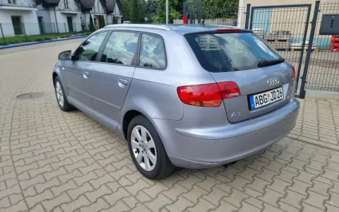 Srebrny Audi A3 kombi zaparkowany na kostce brukowej, w tle domy i drzewa.