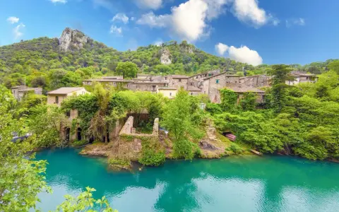 Un borgo incantevole in Umbria, con case in pietra ricoperte di vegetazione che si affacciano su un fiume turchese. Un luogo perfetto per i cammini.