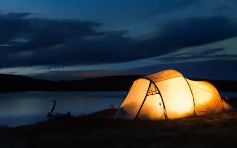 Upplyst tält vid en sjö i skymningen. En cykel står parkerad bredvid. Perfekt för camping Sverige karta-äventyr.
