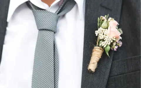 Elegancki krawat do ślubu w kratkę, biała koszula i butonierka z różową różą.