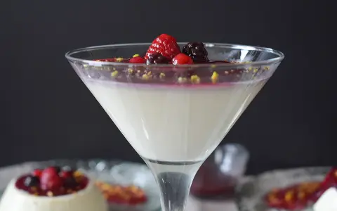 Deliciosa panna cotta receta, cremosa y adornada con frutos rojos y pistachos. Un postre elegante.