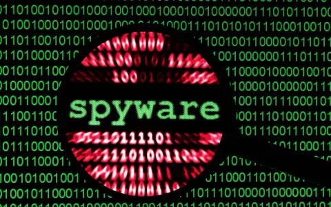 Lupa sobre código binario verde y rojo, con la palabra "spyware" en verde en el centro.