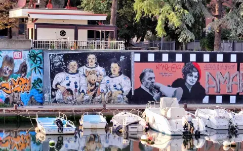 Graffiti colorati sul muro del borgo San Giuliano: astronauti con Alf, personaggi di Amarcord e cani. Barche ormeggiate sull'acqua riflettono i colori.